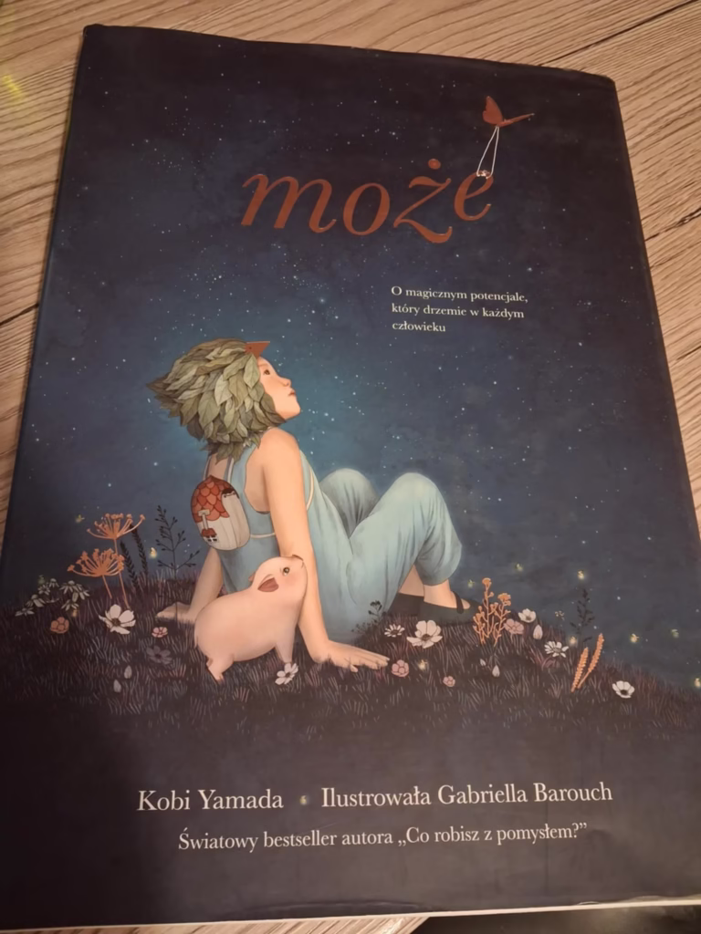 Wiara w siebie – okładka książki „Może” Kobi Yamady. Dziecko w niebieskim stroju siedzi z prosiaczkiem na tle nocnego nieba, symbolizując wiarę w siebie i odkrywanie własnych możliwości.