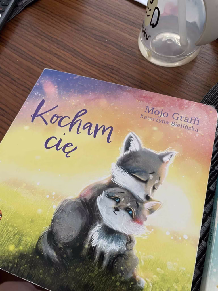 Okładka książki „Kocham cię” autorstwa Mojo Giffin i Katarzyny Bielińskiej, przedstawiająca lisicę tulącą swoje dziecko na tle zachodzącego słońca. Ilustracja symbolizuje miłość, bezpieczeństwo i wsparcie emocjonalne – wartości, które pokazują, jak motywować dziecko bez presji.